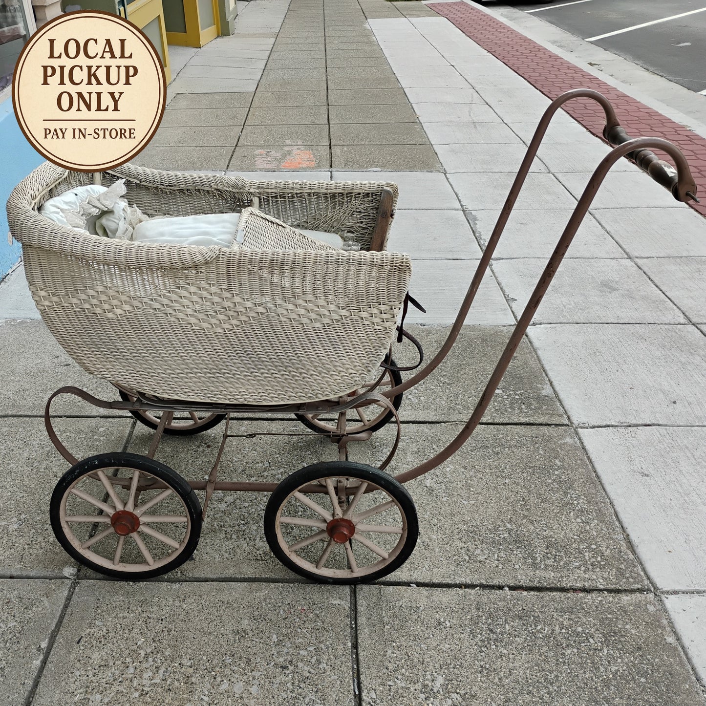 Vintage-style wicker baby buggy on a sidewalk with 'Local Pickup Only' sign.