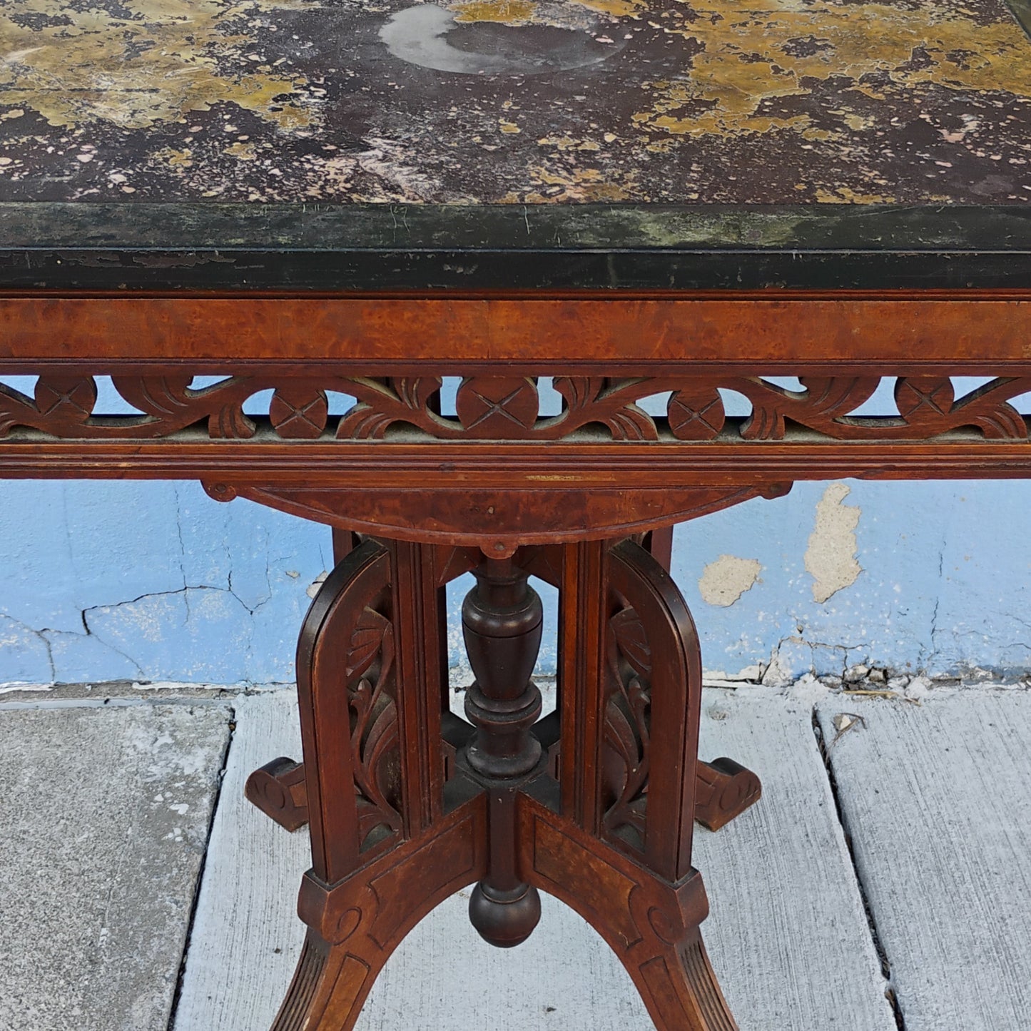 Vintage wooden table with a black marble top against a blue wall.