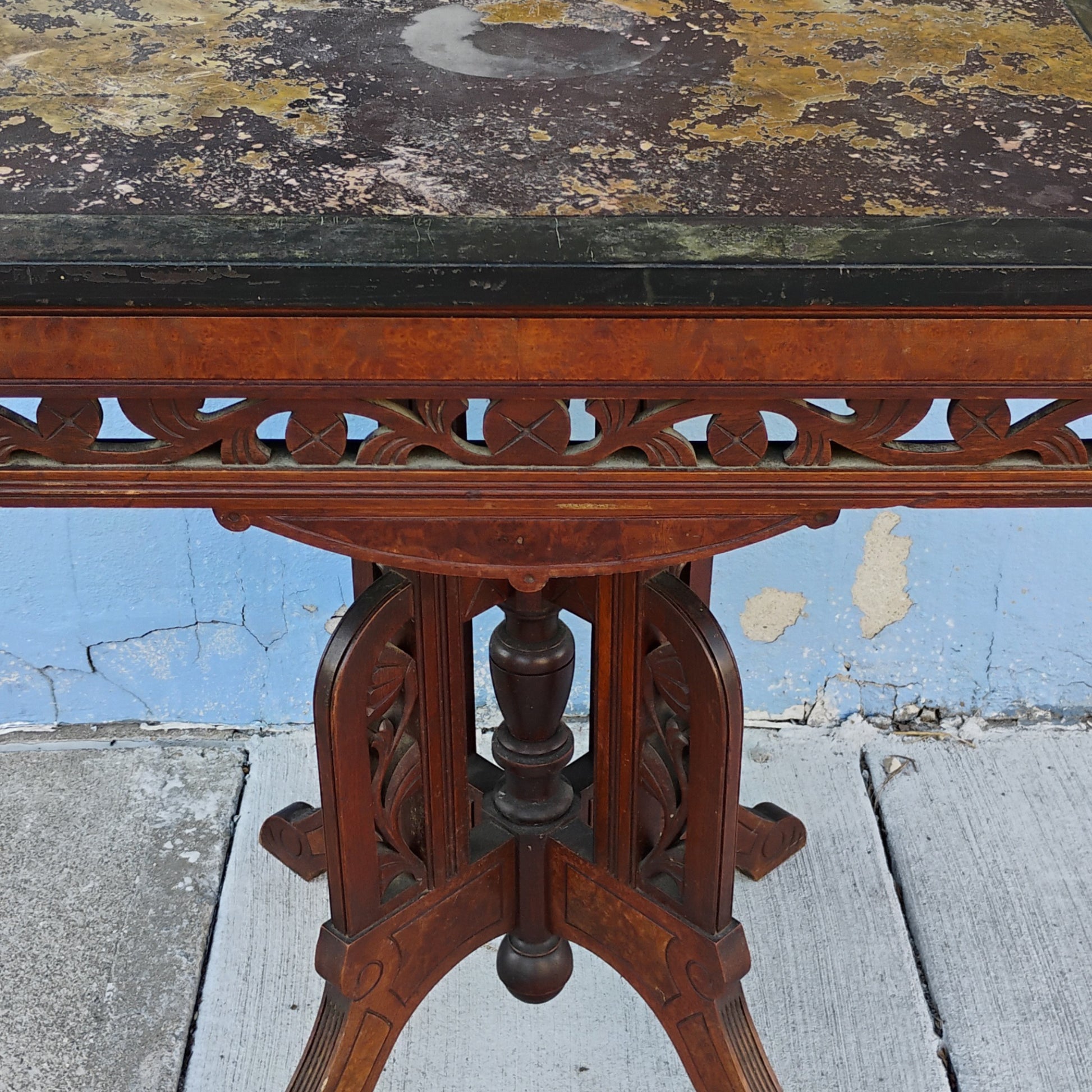 Vintage wooden table with a black marble top against a blue wall.